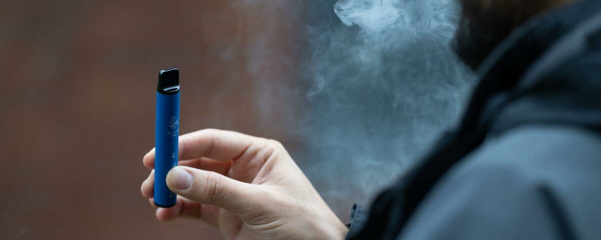 A person holding a vape in their hand with smoke coming out of their mouth