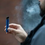 A person holding a vape in their hand with smoke coming out of their mouth