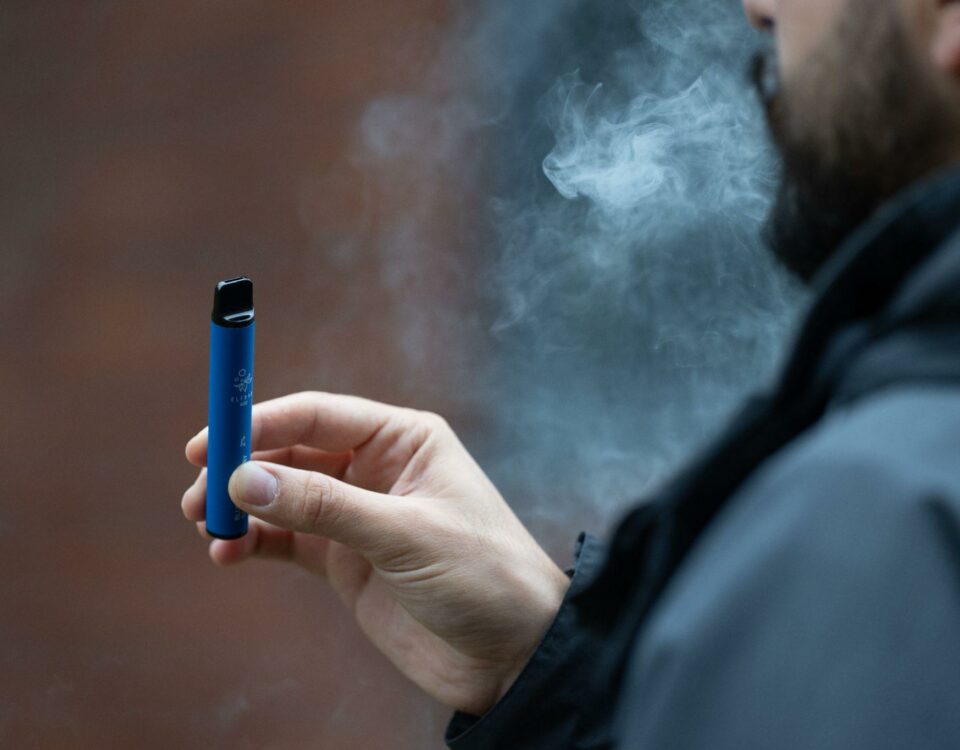A person holding a vape in their hand with smoke coming out of their mouth